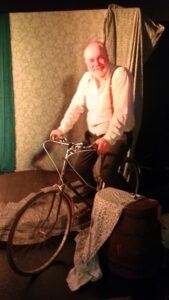 Actor Neil Gore on stage aside old-style bicycle